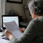 Personne assise devant ordinateur consultant documents financiers retraite.