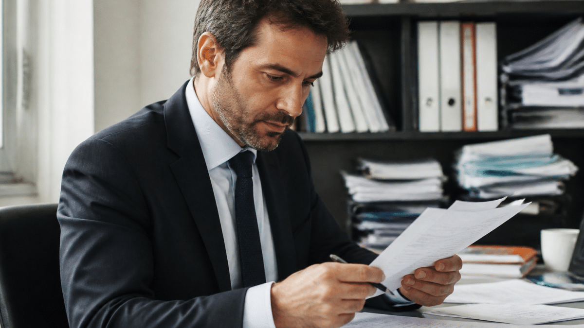 Professionnel en costume consulte documents financiers au bureau.