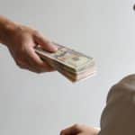 Un homme tend une liasse de billets à une femme assise.