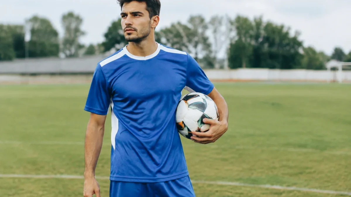 Footballeur debout sur pelouse tenant ballon sous bras