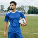 Footballeur debout sur pelouse tenant ballon sous bras
