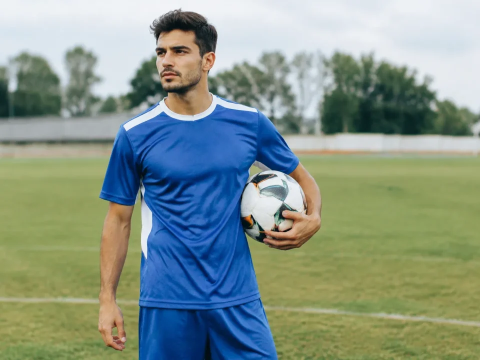 Footballeur debout sur pelouse tenant ballon sous bras