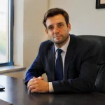 Homme en costume assis derriere un bureau sombre