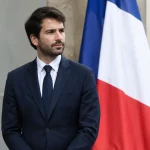 Homme en costume debout devant un drapeau tricolore