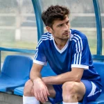 Joueur en maillot assis sur un banc de stade