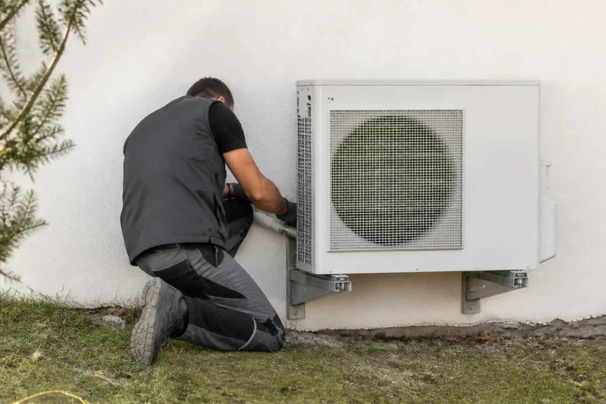 Technicien fixe pompe a chaleur blanche contre un mur